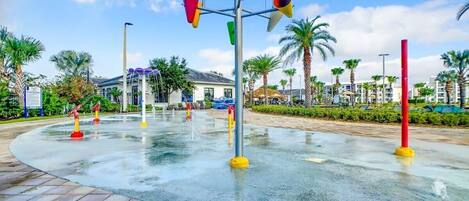 A water feature with colorful buckets and a fountain in a plaza with palm trees and a building in the background.