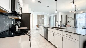 Una cocina moderna con una isla central, electrodomésticos de acero inoxidable e iluminación colgante.