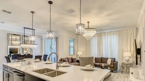 Una cocina moderna con una isla grande, electrodomésticos de acero inoxidable e iluminación colgante.