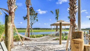 A beach setting with a hammock, wooden chairs, and a gazebo overlooking a lake.
