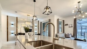 A modern kitchen with a central island, stainless steel appliances, pendant lighting, and a view to the outside.