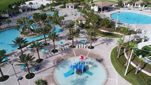 An aerial view of a resort with multiple swimming pools, palm trees, and a central water slide.
