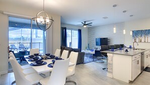 A modern kitchen with a dining area, large windows, and a ceiling fan.