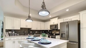 A modern kitchen with white cabinets, stainless steel appliances, and a central island with bar stools. - Last Minute Disney Getaway! Luxury Condo with Private Balcony. Book Now! #87985 (Orlando)