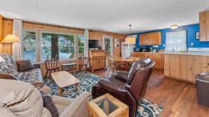 Ein gemütliches Wohnzimmer mit Sofa, Sessel und Couchtisch, ein Essbereich mit Stühlen und eine Küche mit Holzausbau und Kühlschrank.