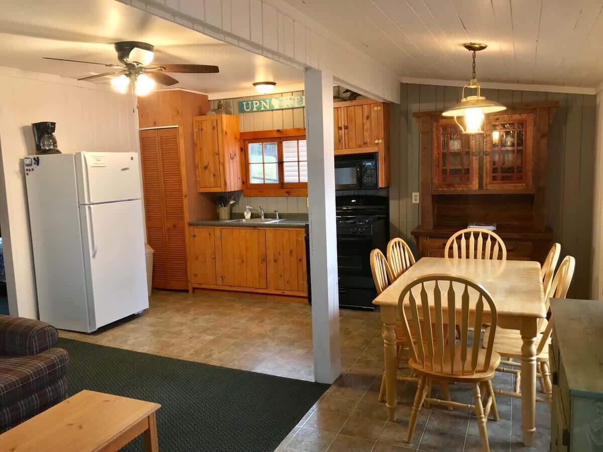 A kitchen with wooden cabinets, a refrigerator, a stove, and a dining table with chairs.