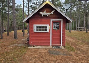 A small red cabin with a white door and window, surrounded by trees. - Loons Landing Legacy (Saint Germain)
