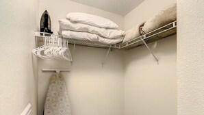 Pequeña habitación cerrada con un radiador blanco, un tendedero portátil y un perchero con ropa doblada y una toalla estampada.