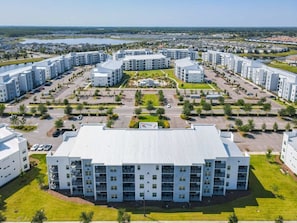 Un immeuble moderne à plusieurs étages, doté d’un toit plat, entouré de zones de stationnement et d’espaces verts.
