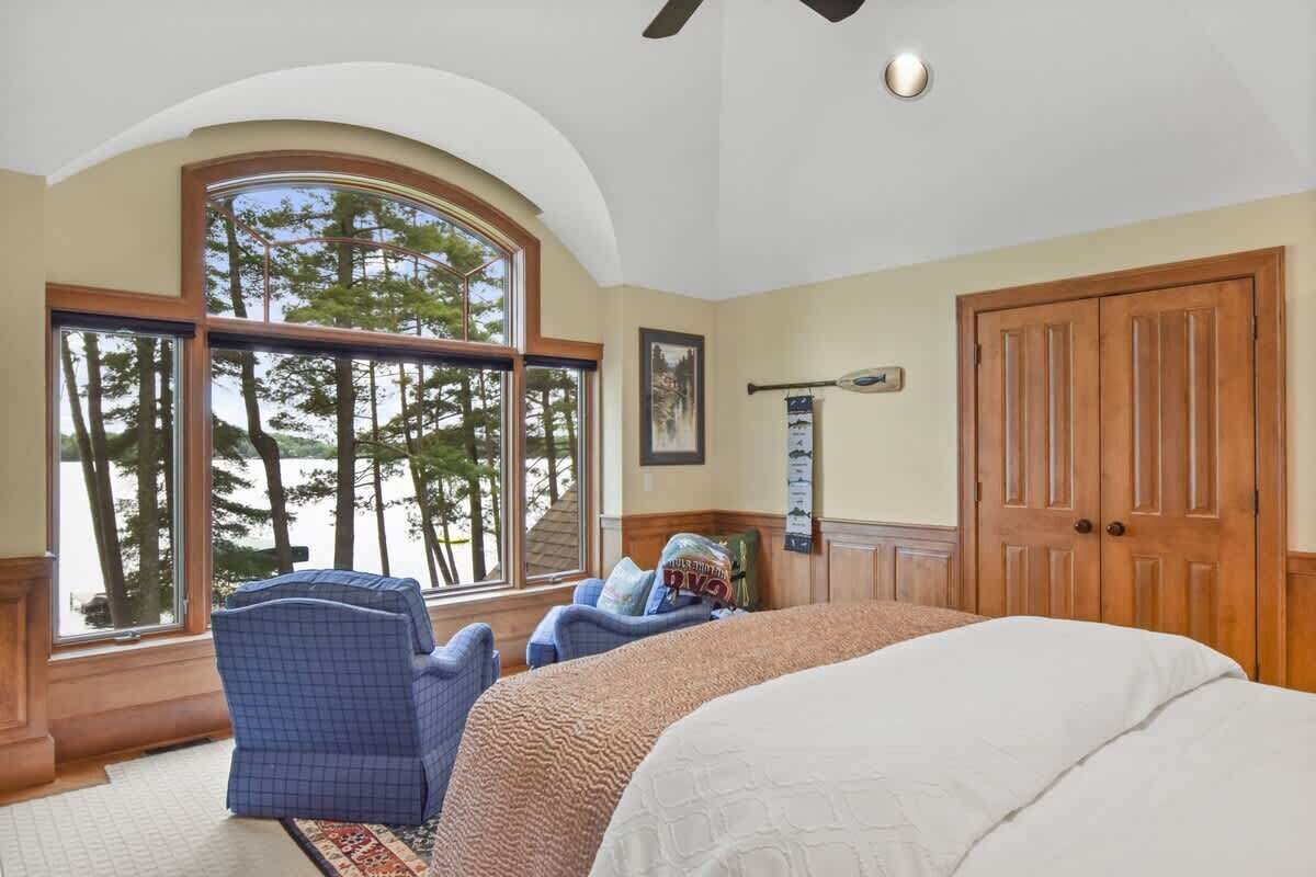 A bedroom with a large window, a bed, a chair, and a wooden door.