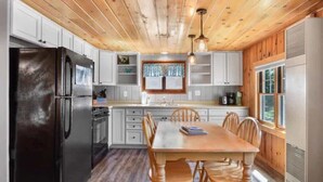 A kitchen with wooden ceiling, white cabinets, a black refrigerator, and a dining table with chairs. - Bayview Resort Waters Edge Cabin 2 (Saint Germain)