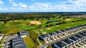 Un parcours de golf avec des bunkers de sable, un quartier résidentiel avec des maisons modernes et un ciel bleu dégagé.