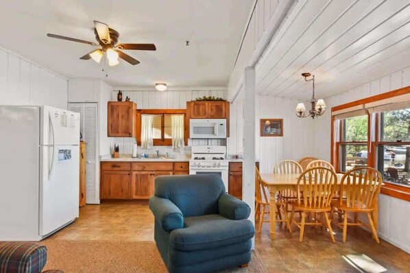 A kitchen with wooden cabinets, a dining table with chairs, a ceiling fan, and a window with a view.