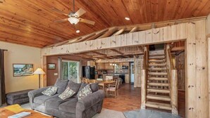 A cozy cabin interior with a wooden ceiling, a sofa, a dining area, and a staircase. - Chain Lake Retreat Holiday Home (Eagle River)