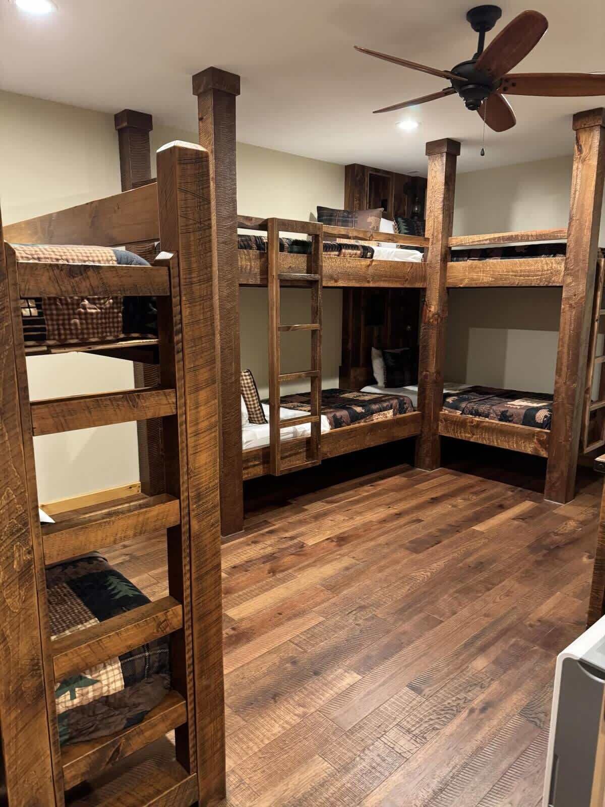 A room with bunk beds, wooden flooring, and a ceiling fan.