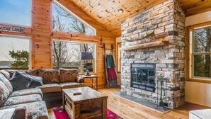 Een gezellig blokhutinterieur met een stenen openhaard, houten wanden en een groot raam met uitzicht op een meer.