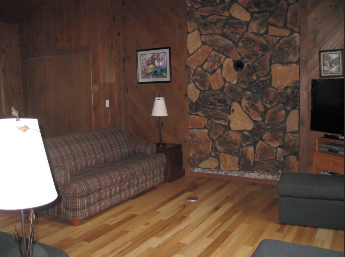 Una sala de estar acogedora con un sofá de cuadros, una lámpara, una pared de piedra y un televisor.