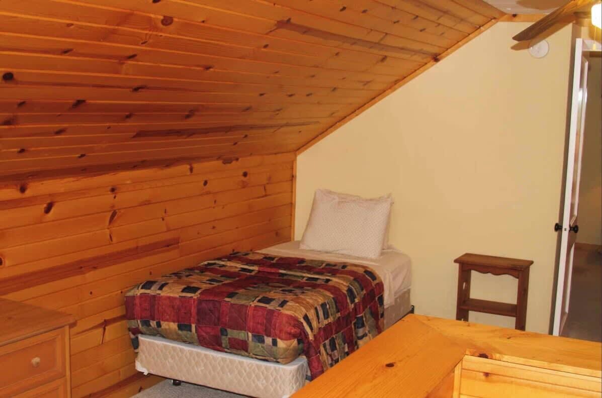 A bedroom with a wooden ceiling, a bed with a quilt, a nightstand, and a small wooden table.