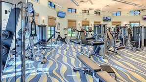Ein großzügiger Fitnessraum mit verschiedenen Trainingsgeräten, großen Fenstern und einem strukturierten Boden.