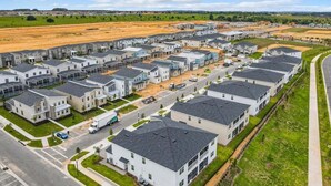 A residential area with modern houses arranged in rows, featuring a central road and green spaces.