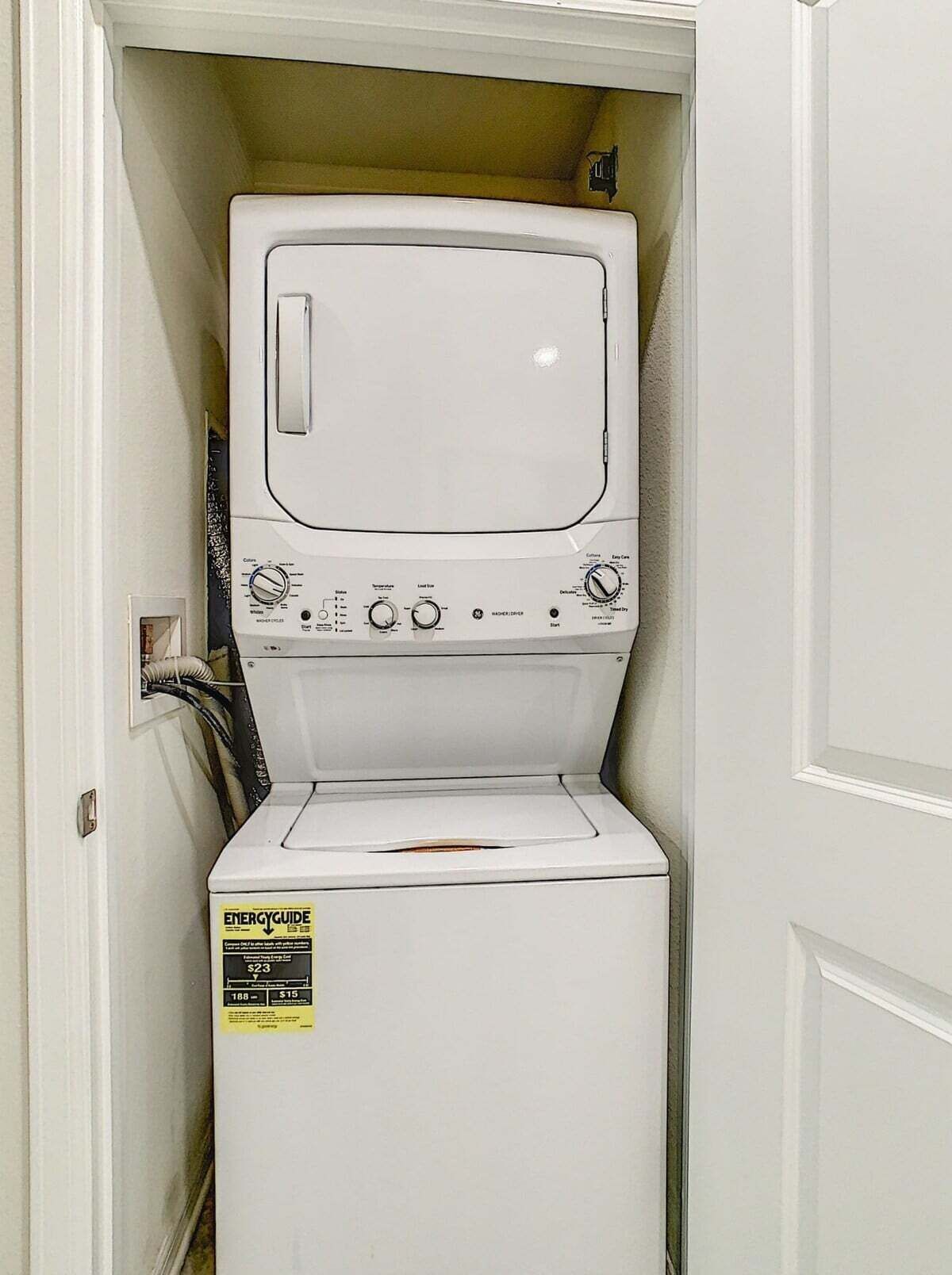 Un appareil compact, blanc, combinant une machine à laver et un sèche-linge à chargement frontal, doté d’un panneau de commande avec de nombreux réglages et d’une étiquette indiquant son niveau d’efficacité énergétique.