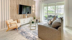 A modern living room with a flat-screen TV, a sofa, a coffee table, and a dining area. - Last Minute Disney Getaway! Themed Bedrooms & Private Balcony. Book Now! #100095 (Orlando)