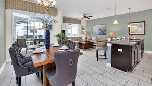 A spacious living area with a dining table, chairs, a kitchen island, and a ceiling fan.