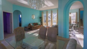A spacious living room with a large glass table, comfortable seating, and a chandelier.
