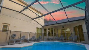 An indoor swimming pool with a glass ceiling, lounge chairs, and a view of the sunset.