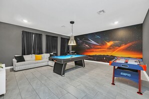 A room with a pool table, sofa, and a space-themed mural on the wall.