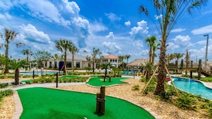 Um campo de golfe com putting green, palmeiras e zona de piscina.
