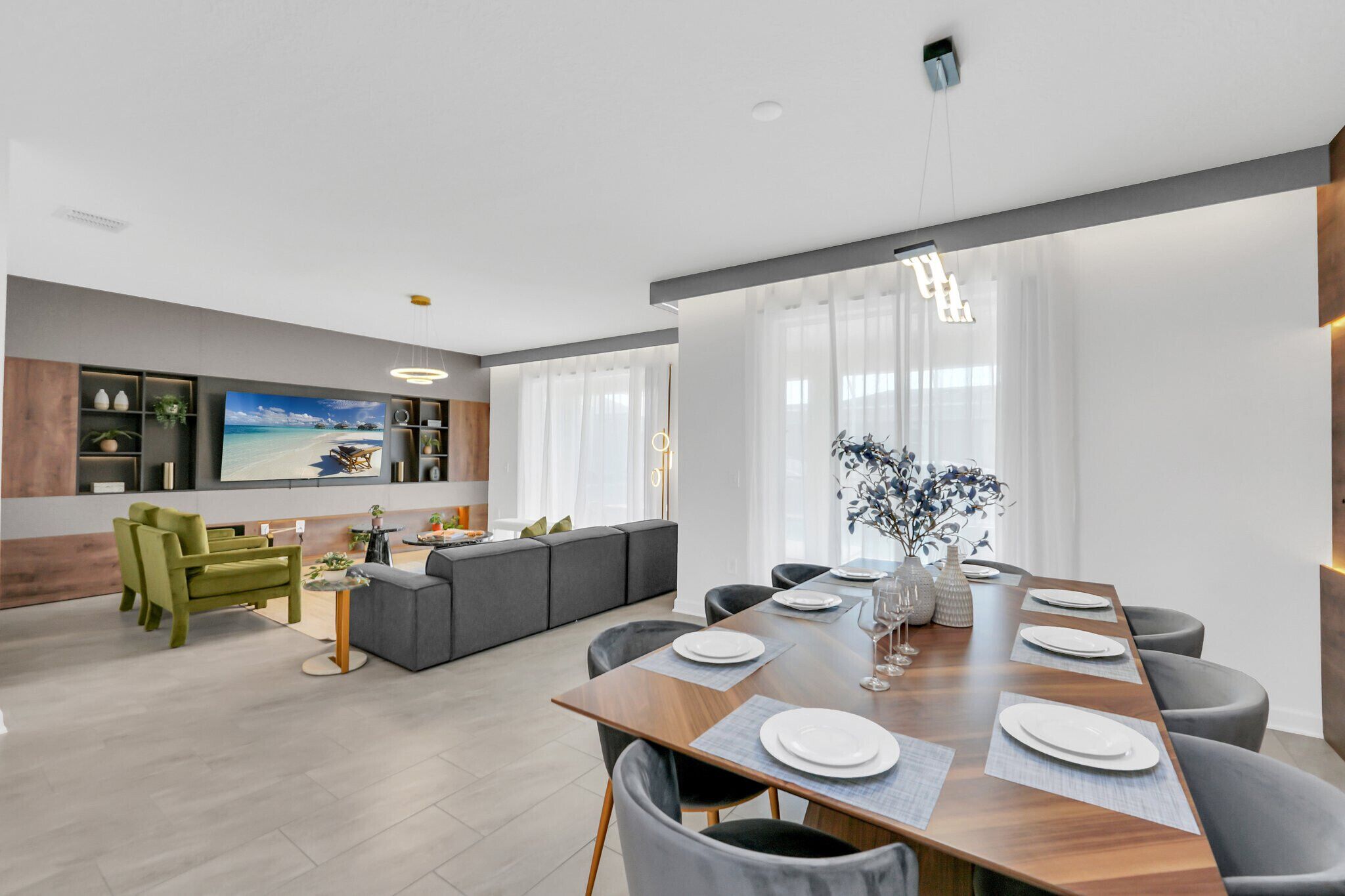 A modern living room with a dining area, featuring a large flat-screen TV, a sofa, and a dining table set for six.