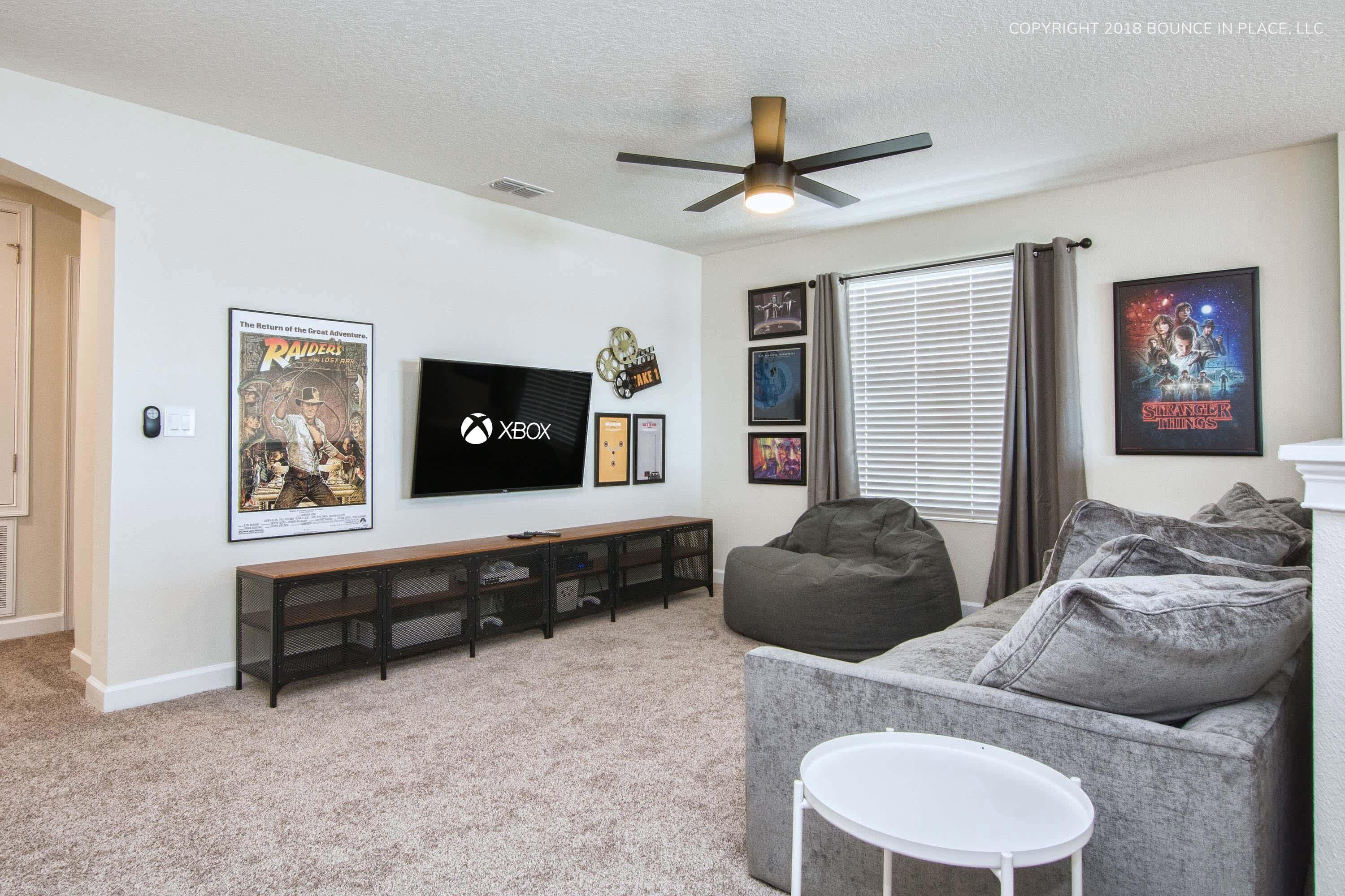 A living room with a flat-screen TV, a ceiling fan, a grey couch, a bean bag, and a coffee table.