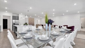A modern kitchen with a central island, a dining area with a glass table, white chairs, and a decorative vase. - Last Minute Disney! Private Pool, Hot Tub, Game Room & Themed Bedrooms. Book Now! #55561 (Orlando)