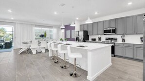 A modern kitchen with grey cabinets, a white island, and bar stools. - Last Minute Disney! Private Pool, Hot Tub, Game Room & Themed Bedrooms. Book Now! #55561 (Orlando)