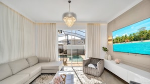 Ein modernes Wohnzimmer mit großem Flachbildfernseher, einer Couch, einem Couchtisch mit Dekoration und Blick auf Pool und Außenbereich.