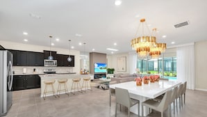 A modern kitchen with dark cabinets, a large island, and a dining area with a white table and chairs. - Last Minute Disney! Private Pool, Hot Tub, Game Room & Themed Bedrooms. Book Now! #55687 (Orlando)