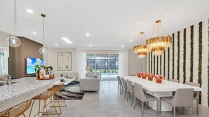 A modern kitchen with a marble countertop, bar stools, and a dining area with a long table and chairs. - Last Minute Disney! Private Pool, Hot Tub, Game Room & Themed Bedrooms. Book Now! #55687 (Orlando)