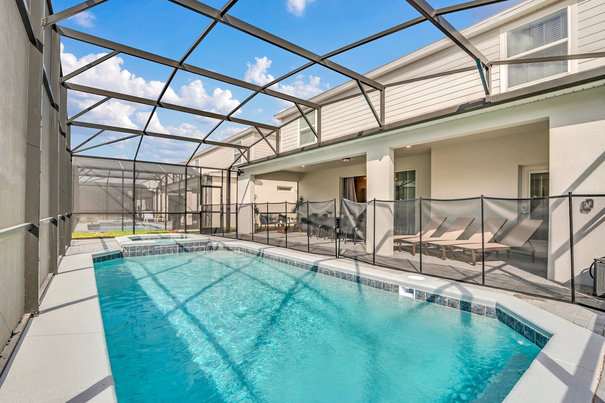 Ein Schwimmbad mit Glasveranda, Liegestühlen und blauem Himmel.