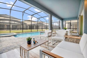 Een overdekt terras met een zwembad, tuinmeubilair en uitzicht op de achtertuin.