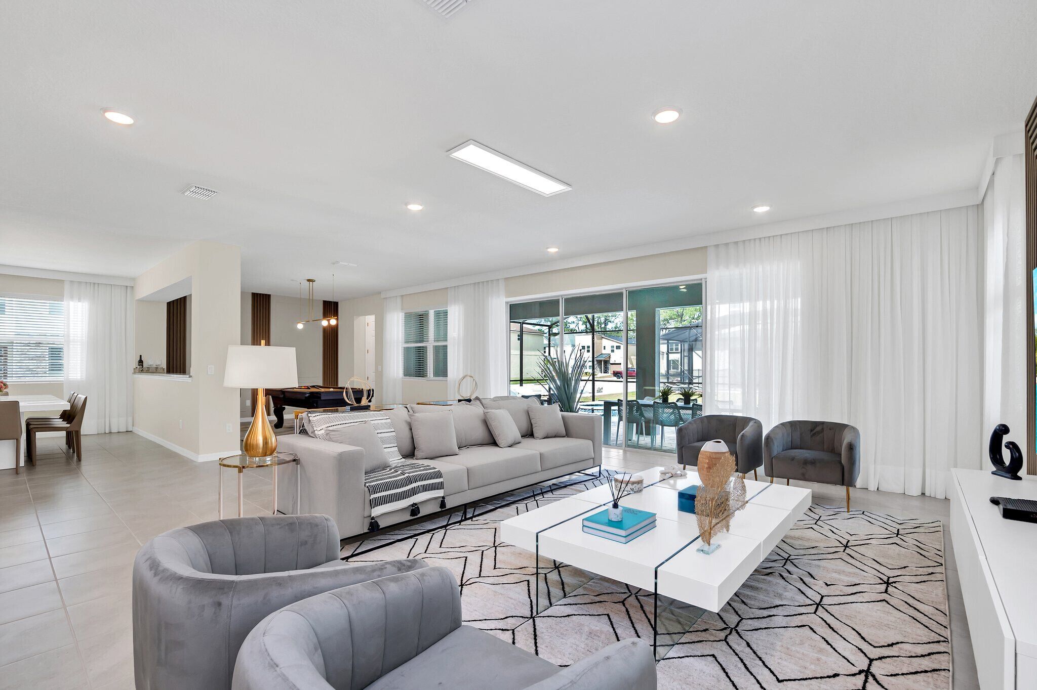 A modern living room with a sofa, armchairs, a coffee table, and a dining area with a table and chairs.