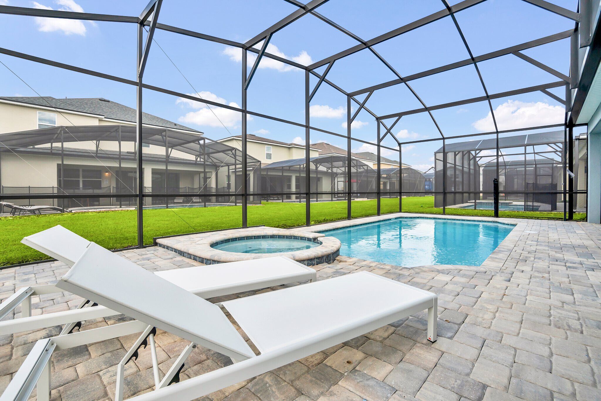 A pool area with a hot tub, lounge chairs, and a covered patio.