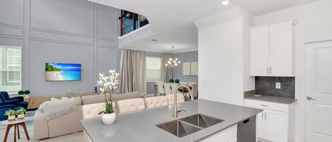 A modern kitchen with a central island, white cabinetry, and a dining area with a sofa and chairs.