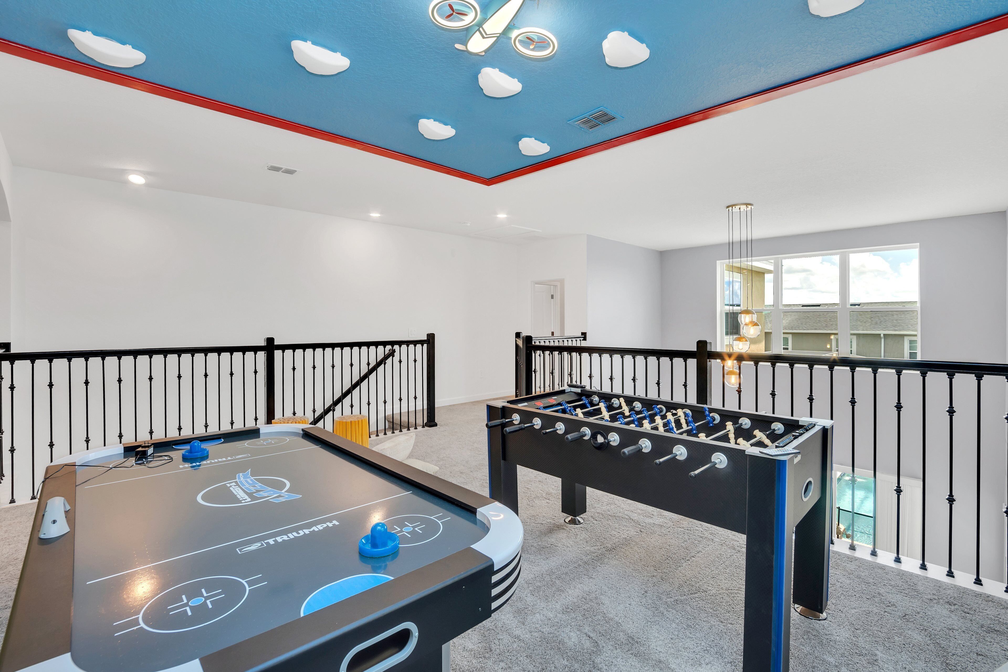 Una habitación con mesa de fútbol de mesa y mesa de shuffleboard, un balcón con barandilla y un ventanal con vistas.