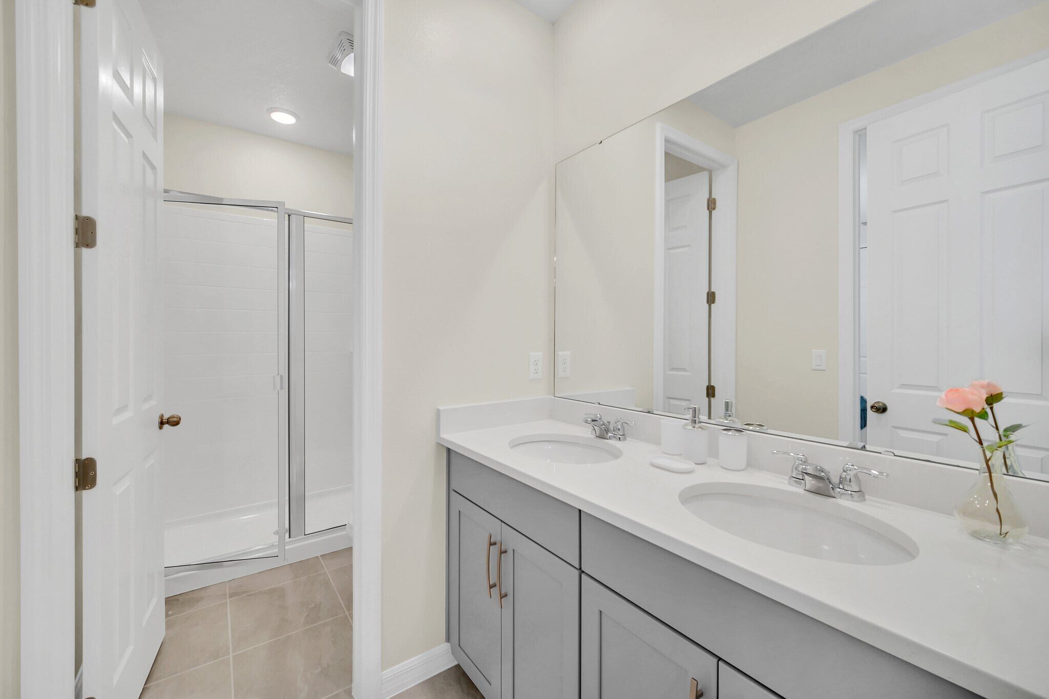 A modern bathroom with two sinks, a large mirror, and a shower area.