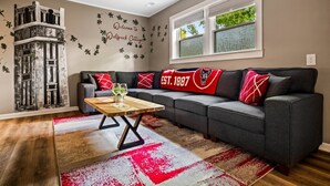 Ein Wohnzimmer mit einem Ecksofa, einem Couchtisch, einer Wand mit Dekoration und einem Fenster mit Jalousien.