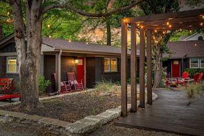 Un espacio al aire libre cubierto con una terraza de madera, sillas rojas y luces colgantes.