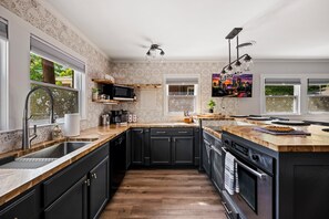 A modern kitchen with dark cabinetry, a wooden countertop, a built-in oven, and a large island.