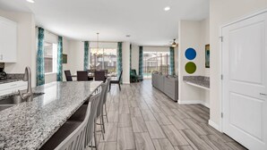 A modern kitchen with granite countertops, a dining area with a table and chairs, and a view of the outdoors through large windows.