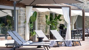 A sunlit outdoor lounge area with lounge chairs and a table, covered by a canopy and curtains, set against a stone wall. - Villa in Terontola with 3 bedrooms sleeps 6 (Terontola)